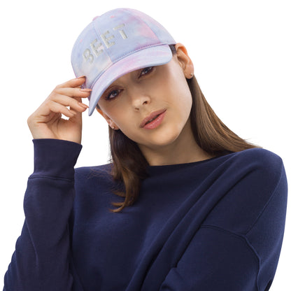 Woman showing BEET tie dye baseball cap featuring vibrant, multi-colored patterns with the BEET logo on the front.